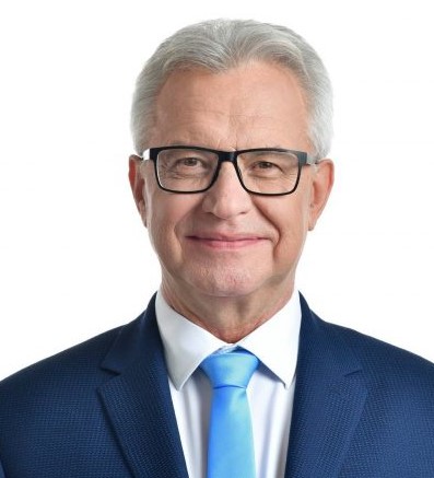 Przystojny, uśmiechnięty mężczyzna w okularach. Ubrany w białą koszulę z krawatem i granatowy garnitur. Prezes PFRON Krzysztof Michałkiewicz